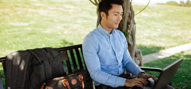 Man sitting on a park bench and working on a laptop